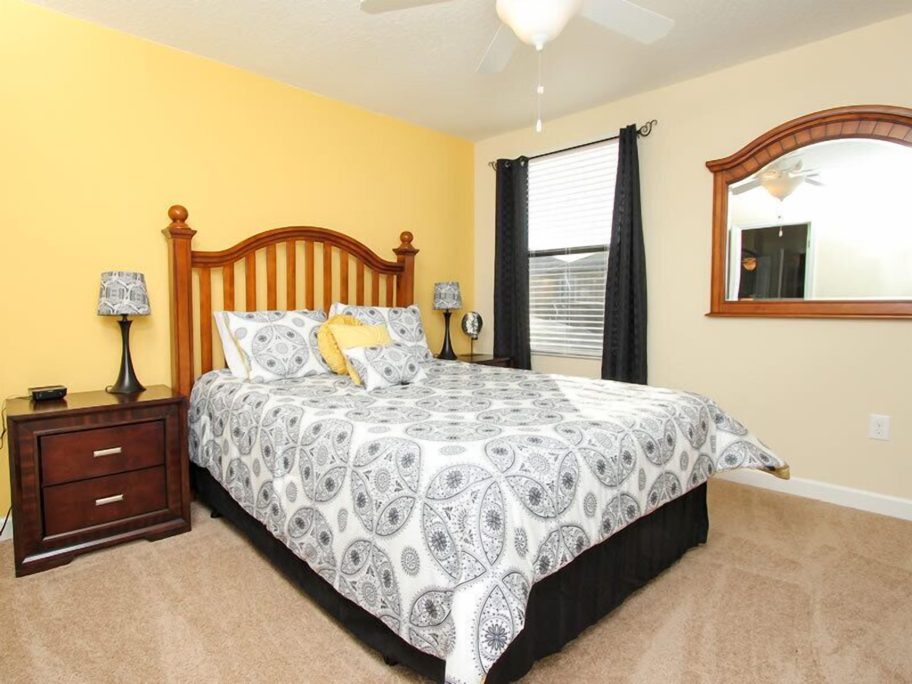 A bedroom with a bed, nightstands, a mirror, and a ceiling fan.