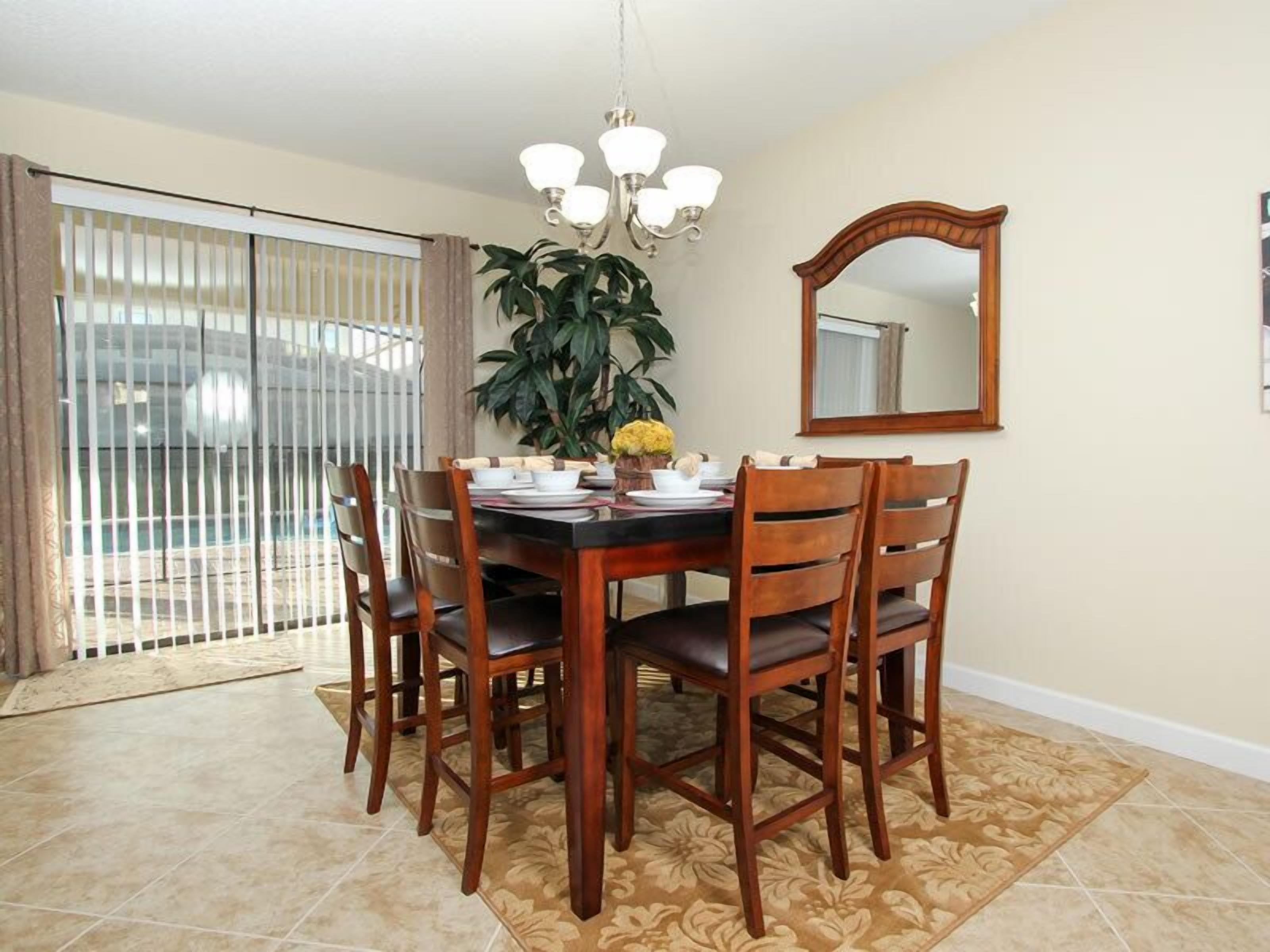A dining area with a wooden table, chairs, a chandelier, a large mirror, and a potted plant.