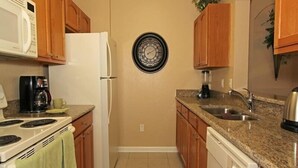 A compact kitchen with wooden cabinets, a white refrigerator, a microwave, a stove, a sink, and a clock on the wall. - Ov2939 - Windsor Hills Resort - 3 Bed 2 Baths Townhome (Kissimmee)