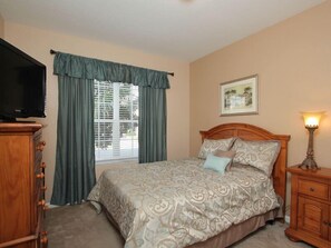A bedroom with a bed, a television, a window with curtains, a bedside lamp, and a framed picture on the wall. - Ov2929 - Windsor Hills Resort - 5 Bed 5 Baths Villa (Kissimmee)