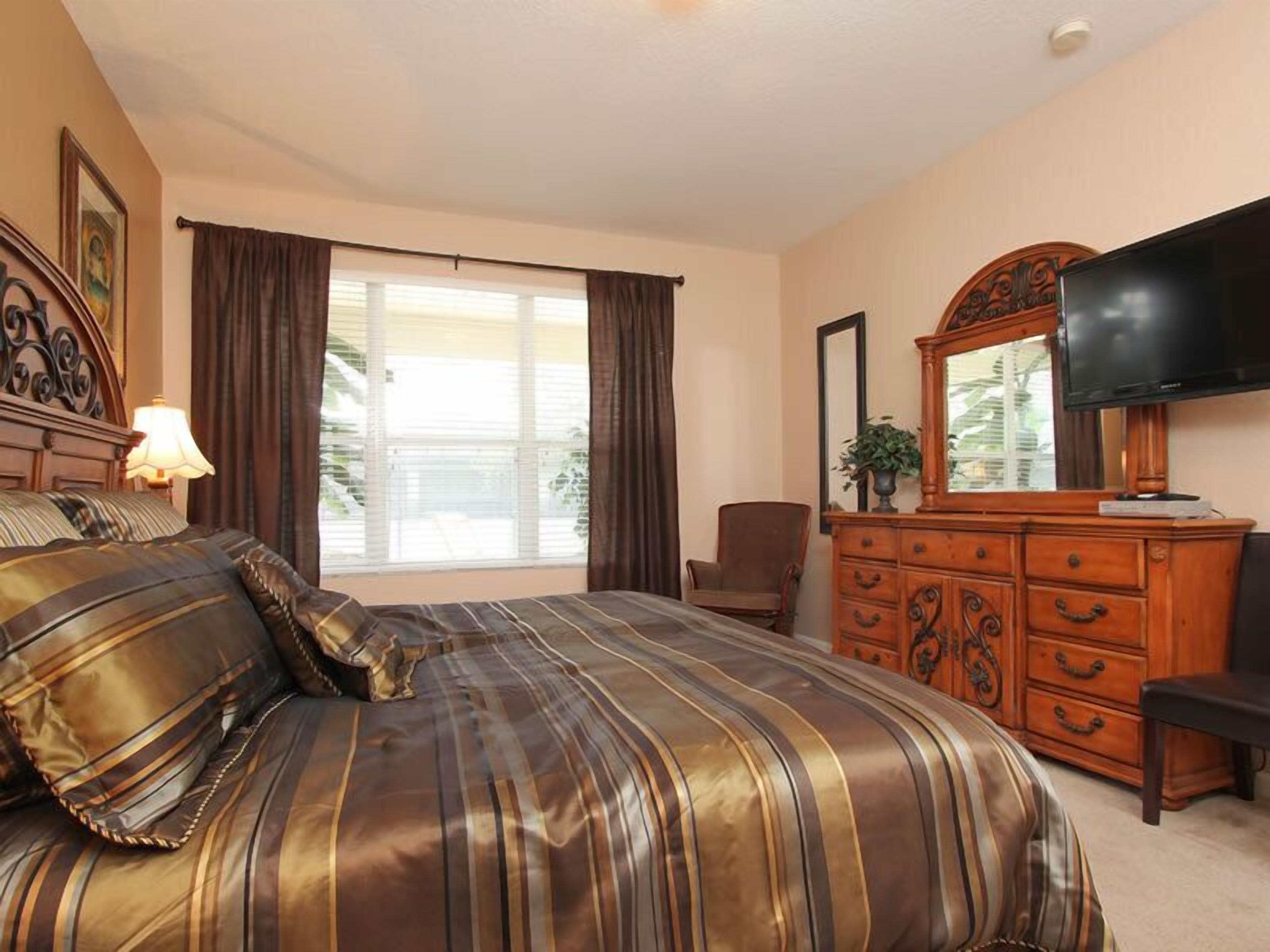 A bedroom with a large bed, a dresser, a chair, a television, and a window with curtains.