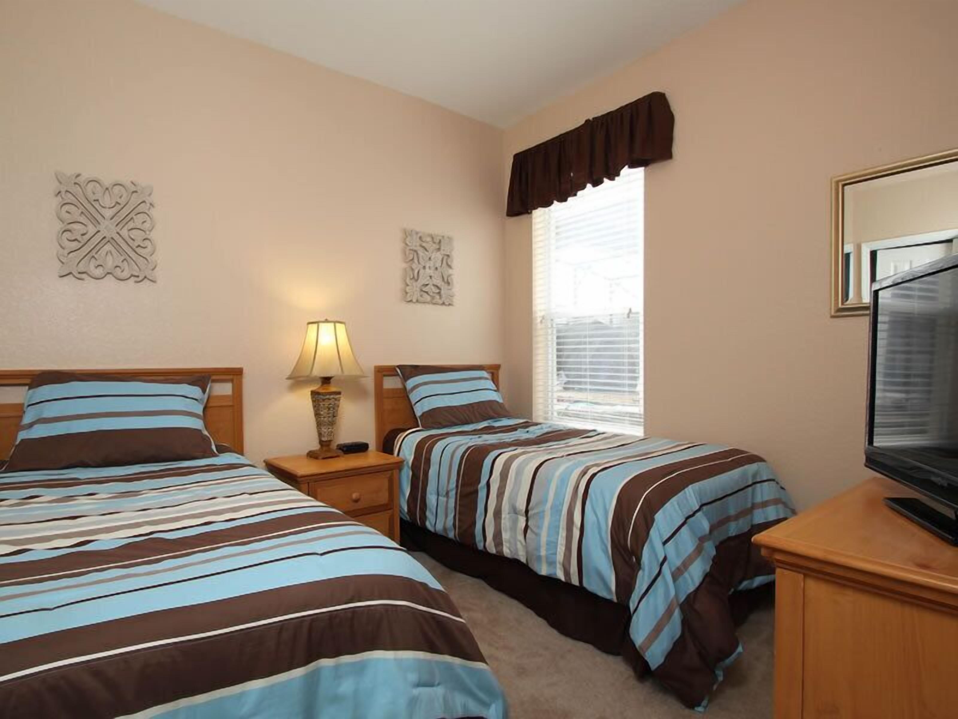 A hotel room with two beds, a TV, and a window with blinds.