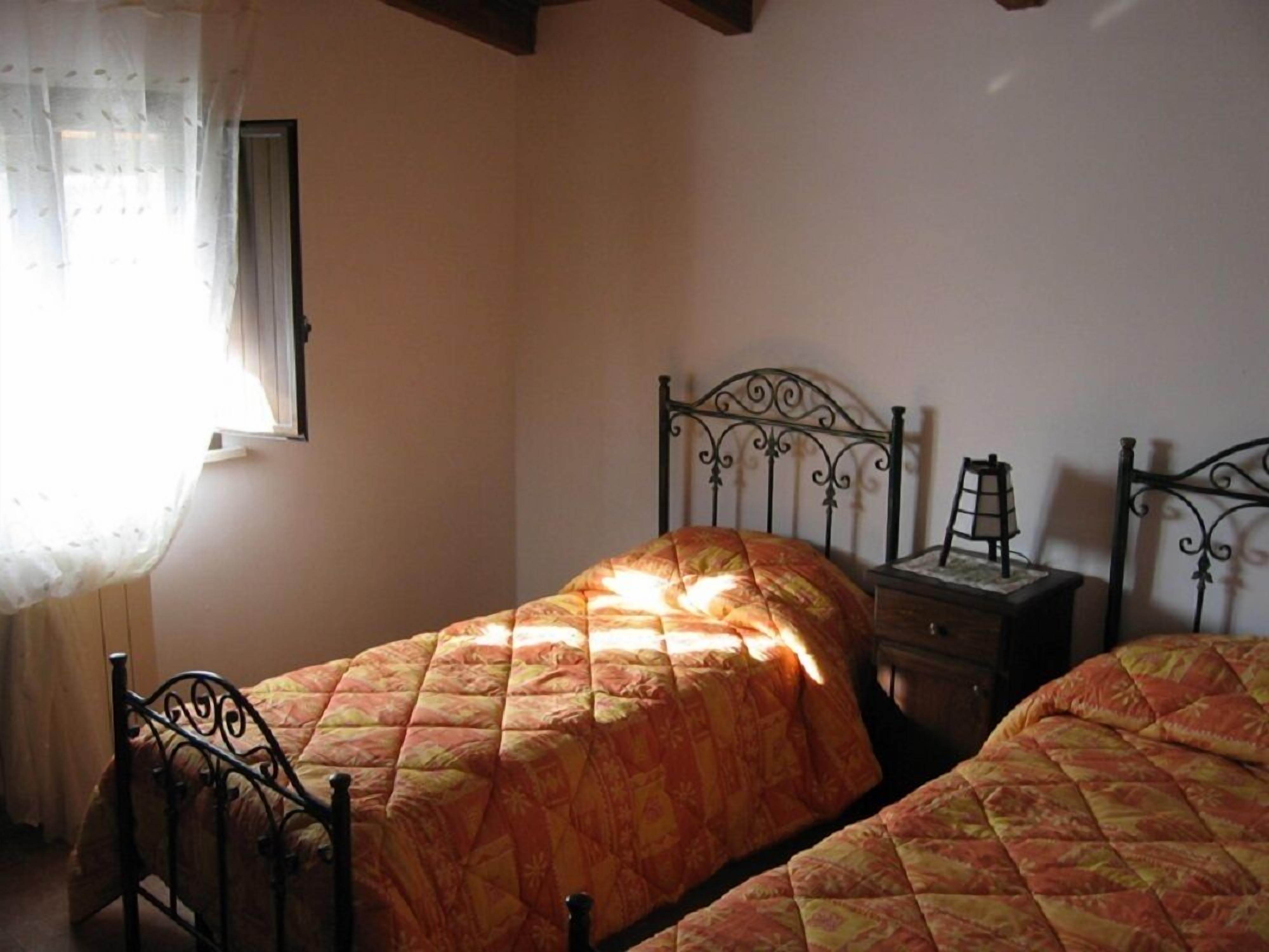 Un dormitorio con dos camas, una mesita de noche y una ventana con cortina translúcida.
