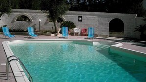 Une piscine à l’eau claire, entourée de chaises longues et d’un mur de pierre.