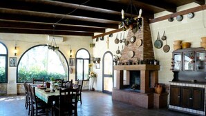 Une cuisine rustique avec une cheminée en briques, des ustensiles de cuisine suspendus et un coin repas comprenant une table et des chaises.