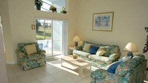 A living room with floral-patterned sofas and a coffee table, a sliding glass door leading to a patio, and a framed picture on the wall. - Ov2942 - Indian Creek - 4 Bed 3 Baths Villa (Kissimmee)