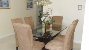 A dining table with a glass top surrounded by six beige chairs, a chandelier, and a vase with flowers. - Ov2942 - Indian Creek - 4 Bed 3 Baths Villa (Kissimmee)