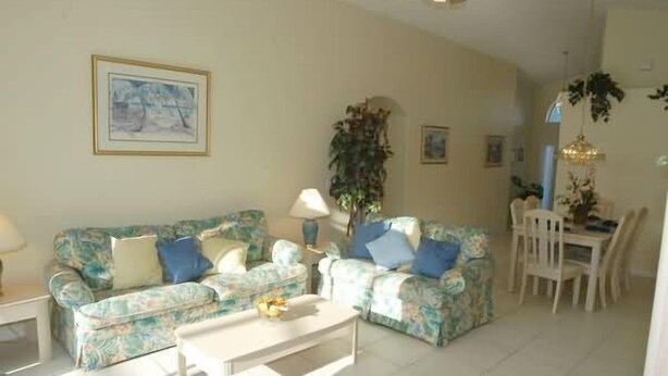 A living room with floral-patterned sofas, a coffee table, and a dining area with a table and chairs. - Ov2942 - Indian Creek - 4 Bed 3 Baths Villa (Kissimmee)