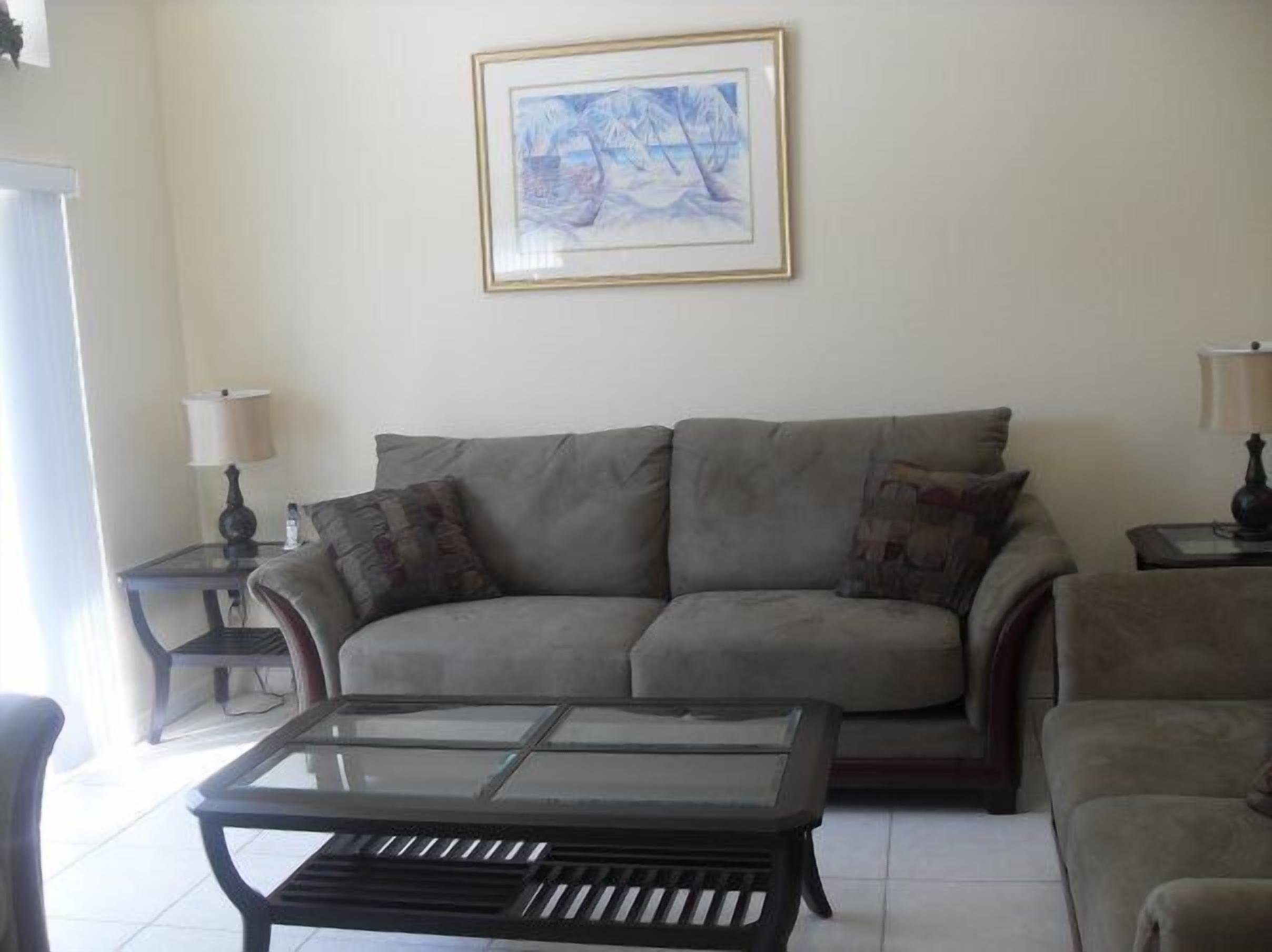 A living room with a grey sofa, a glass-top coffee table, and a framed picture on the wall.