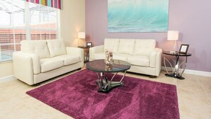 Una sala de estar con dos sofás blancos, una mesa de centro redonda, un tapete morado, un cuadro grande de una ola y una pared a rayas coloridas.