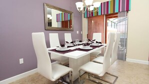 Comedor con una mesa blanca para cuatro, sillas blancas, una araña y un tapiz de pared a rayas coloridas.