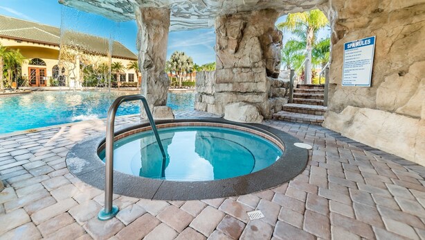Un jacuzzi bajo una formación rocosa con una piscina al fondo.