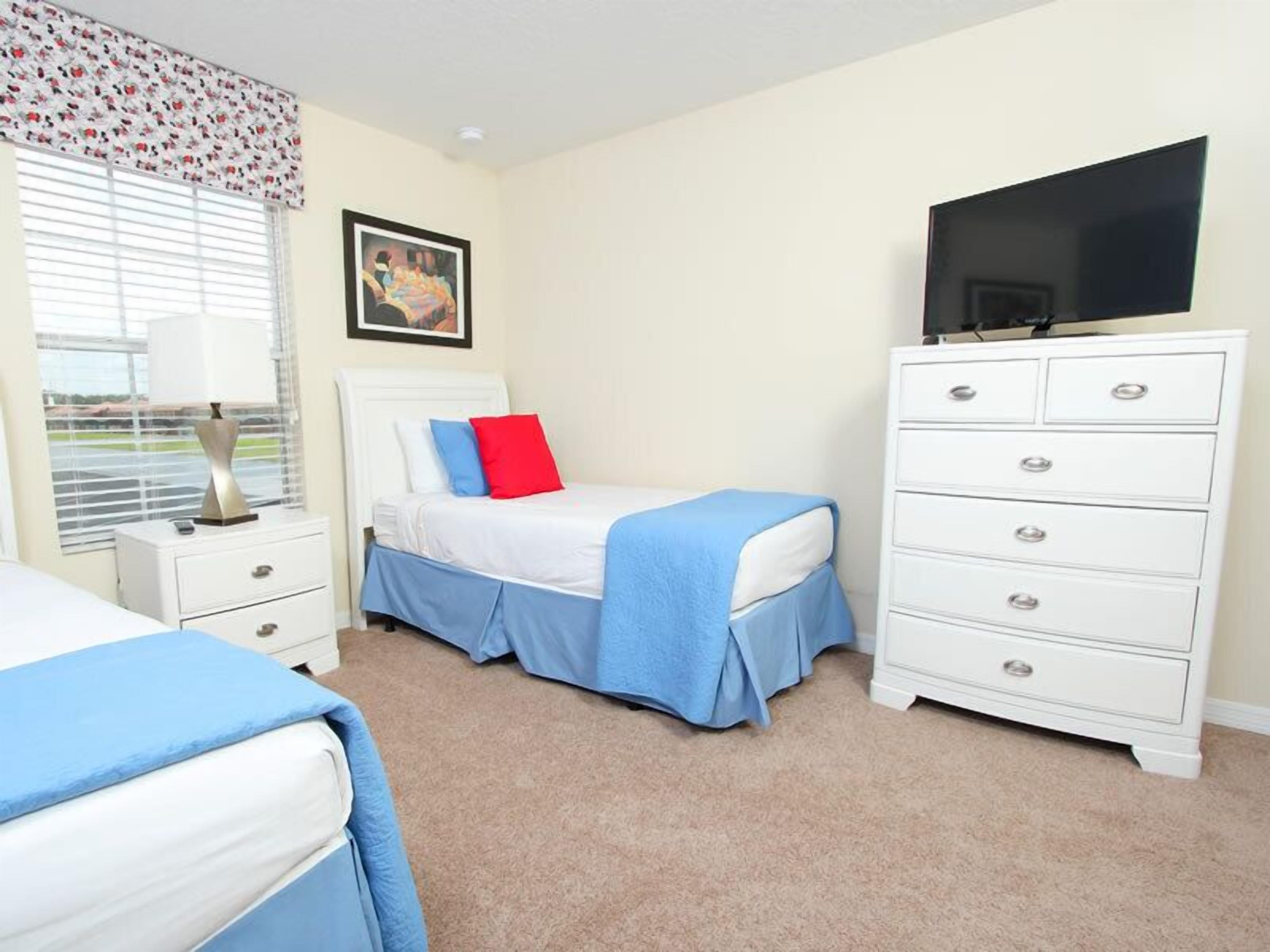 A bedroom with a bed, a dresser, a television, and a window with blinds.