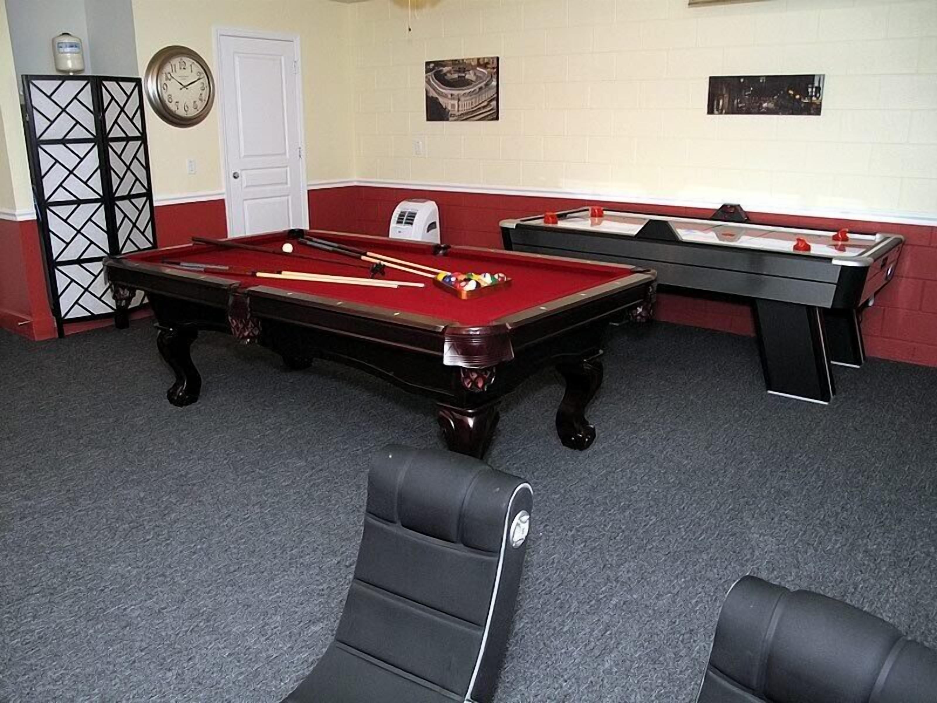 A pool table with cues and balls, a clock, and a small heater on the wall.