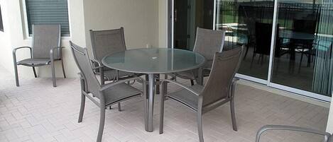A patio with a glass table and six chairs, a sliding glass door, and a view of a residential area.