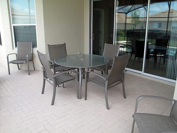 A patio with a glass table and six chairs, a sliding glass door, and a view of a residential area.