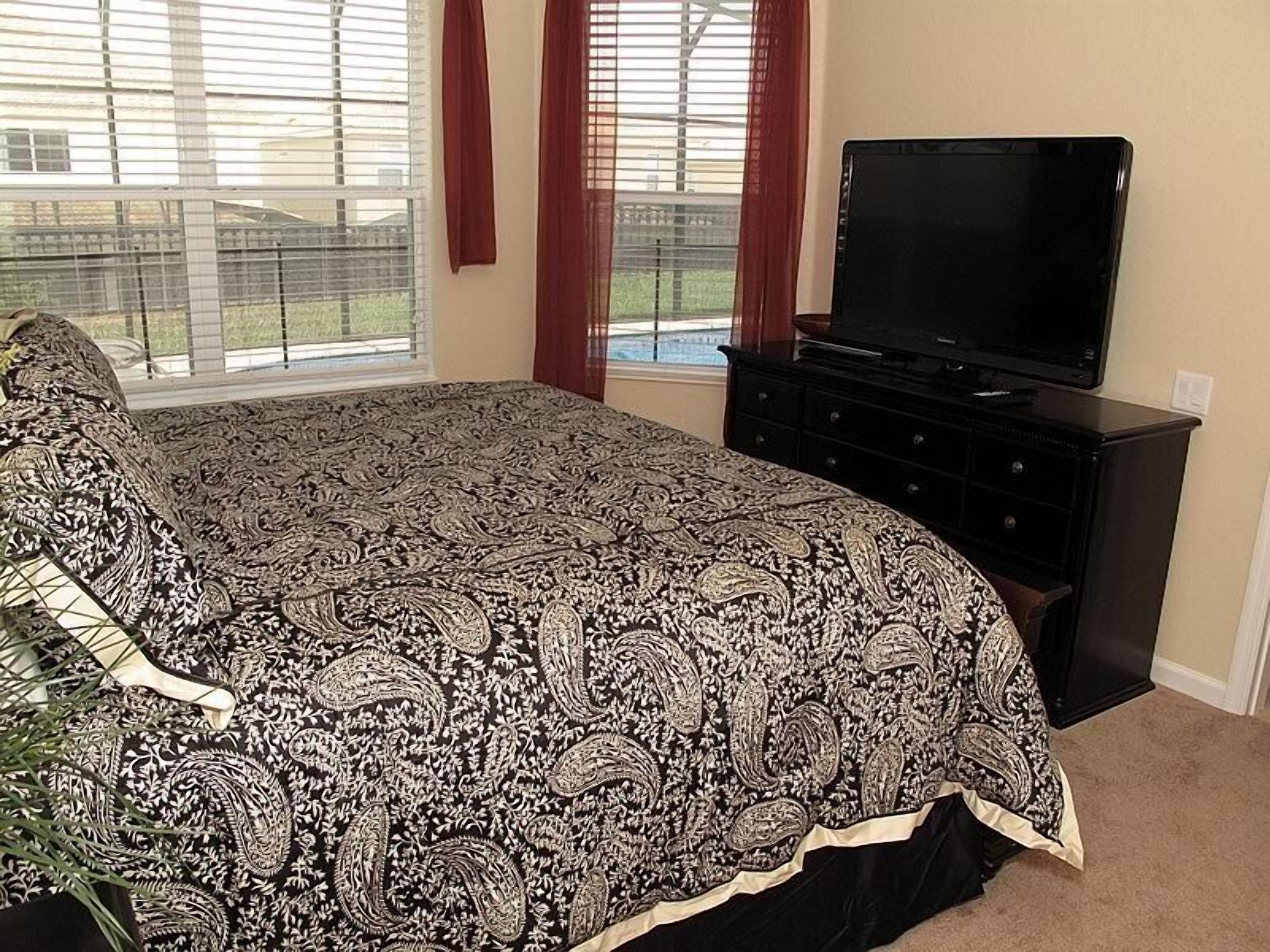 A bedroom with a large bed, a dresser, a TV, and a window with curtains.