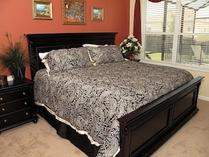 A bedroom with a large bed, dark wooden headboard, and a window with blinds.