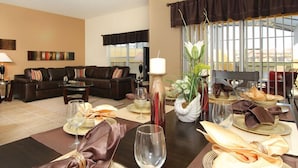 A dining area with a table set for four, a sofa in the background, and a window with a view.