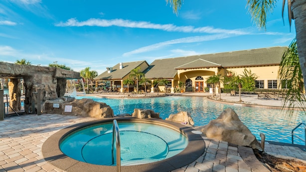 A pool area with a hot tub, lounge chairs, and a building with a tiled roof.