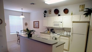 A kitchen with white cabinets, a central island, a stove, and a refrigerator. There are plants on the island and a window with blinds. - Ov2935 - Windsor Hills Resort - 5 Bed 5 Baths Villa (Kissimmee)