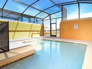 An indoor swimming pool with clear glass walls, a view of the sky, and a sign indicating pool rules.