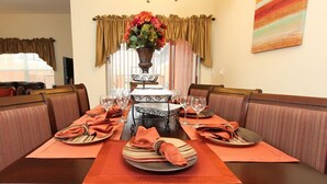 Comedor con una larga mesa dispuesta para seis personas, rodeada de asientos acolchados, un candelabro y un florero.