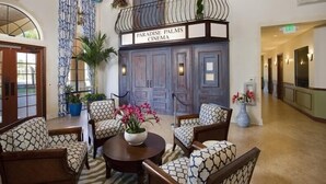 A lobby with a sign reading "Paradise Palms Cinema," featuring a balcony with plants, patterned chairs, and ceiling fans.