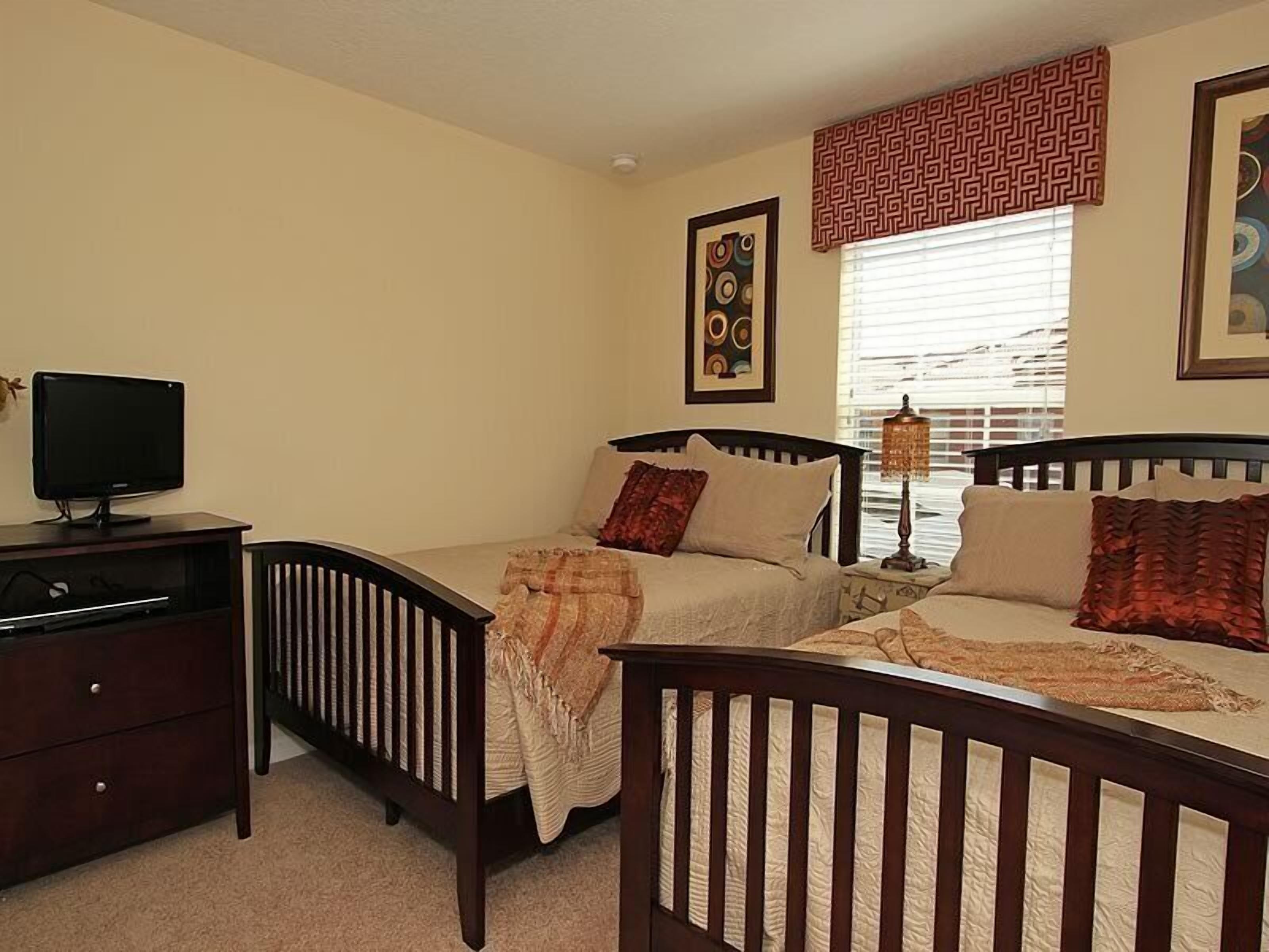 A bedroom with two single beds, a TV on a dresser, and a window with patterned curtains.