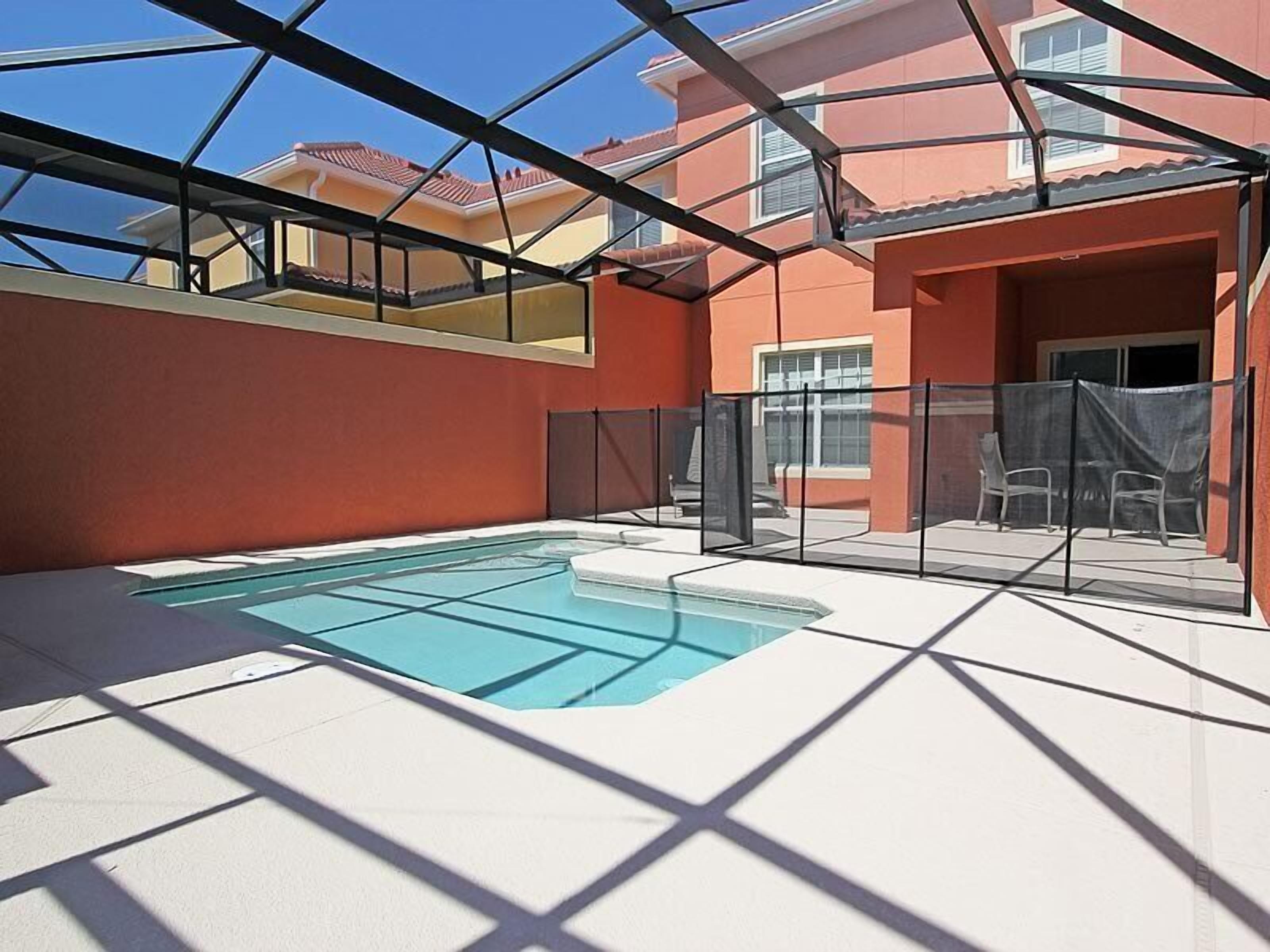 Una piscina con fondo de cristal, rodeada por un porche cubierto con sillas y una valla.