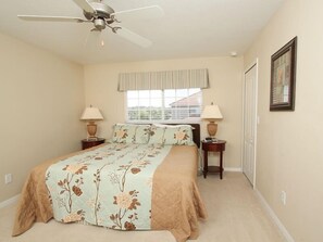 A bedroom with a bed, two bedside tables, a ceiling fan, a window with blinds, and a framed picture on the wall.