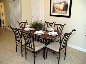 A dining room with a round glass table set for six, surrounded by six wooden chairs with cushioned seats.