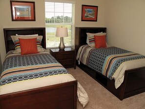 A hotel room with two beds, each with a patterned bedspread and pillows, a nightstand with a lamp, and two framed pictures on the wall.