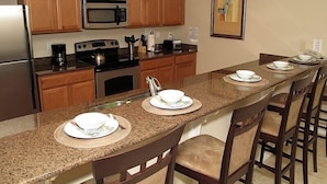 Una cocina con armarios de madera, microondas, estufa y un lavamanos. Hay sillas alrededor de la isla y un cuadro en la pared.