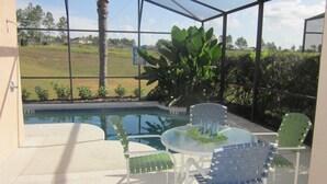 Uma área externa coberta com piscina, mesa e cadeiras, e uma planta grande.