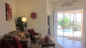 Sala de estar com sofá, poltrona, mesa de centro, uma planta e vista exterior por uma porta de vidro.