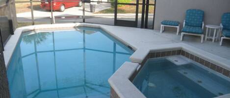A swimming pool area with a hot tub, lounge chairs, and a view of a residential street.