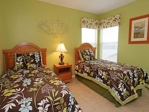 A room with two beds, a nightstand with a lamp, a decorative wall piece, and a window with curtains.