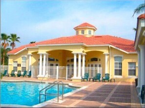 A yellow building with a red roof, a swimming pool, and a covered patio area with chairs. - Ov2644 - Emerald Island - 3 Bed 2.5 Baths Townhome (Kissimmee)