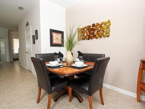 Un coin repas comprenant une table en bois, quatre chaises noires, un vase avec une plante et un élément décoratif mural.