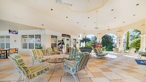 A spacious indoor area with multiple seating arrangements, including striped chairs and a round table. There are signs for a restaurant and a bar, and the area is well-lit with ceiling lights. - Ov2563 - Windsor Hills Resort - 3 Bed 3 Baths Townhome (Kissimmee)