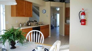 A kitchen with wooden cabinets, a dining table with chairs, a clock, and a fire extinguisher. - Ov2682 - Espirit - 4 Bed 2.5 Baths Villa (Davenport)