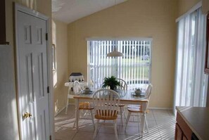 Uma área de refeições com mesa e cadeiras, uma janela com persianas e uma porta.