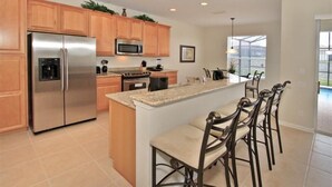 A modern kitchen with a stainless steel refrigerator, a microwave, and a large island with bar stools. - Ov2658 - Windsor Hills Resort - 5 Bed 5 Baths Villa (Kissimmee)