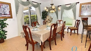 Ein Esszimmer mit einem für sechs Personen gedeckten Tisch, Holzsesseln, einer Kristallleuchtre und Vorhängen.