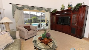 Ein Wohnzimmer mit einem beigefarbenen Sofa, einem Glastisch und einer Holzkommode mit einem Fernseher.