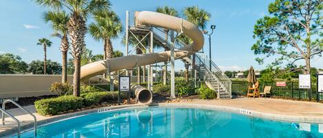 A pool with a water slide, palm trees, and a no diving sign.