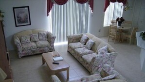 Ein Wohnzimmer mit Sofas mit floralem Muster, einem Couchtisch und einem Essbereich mit Tisch und Stühlen.