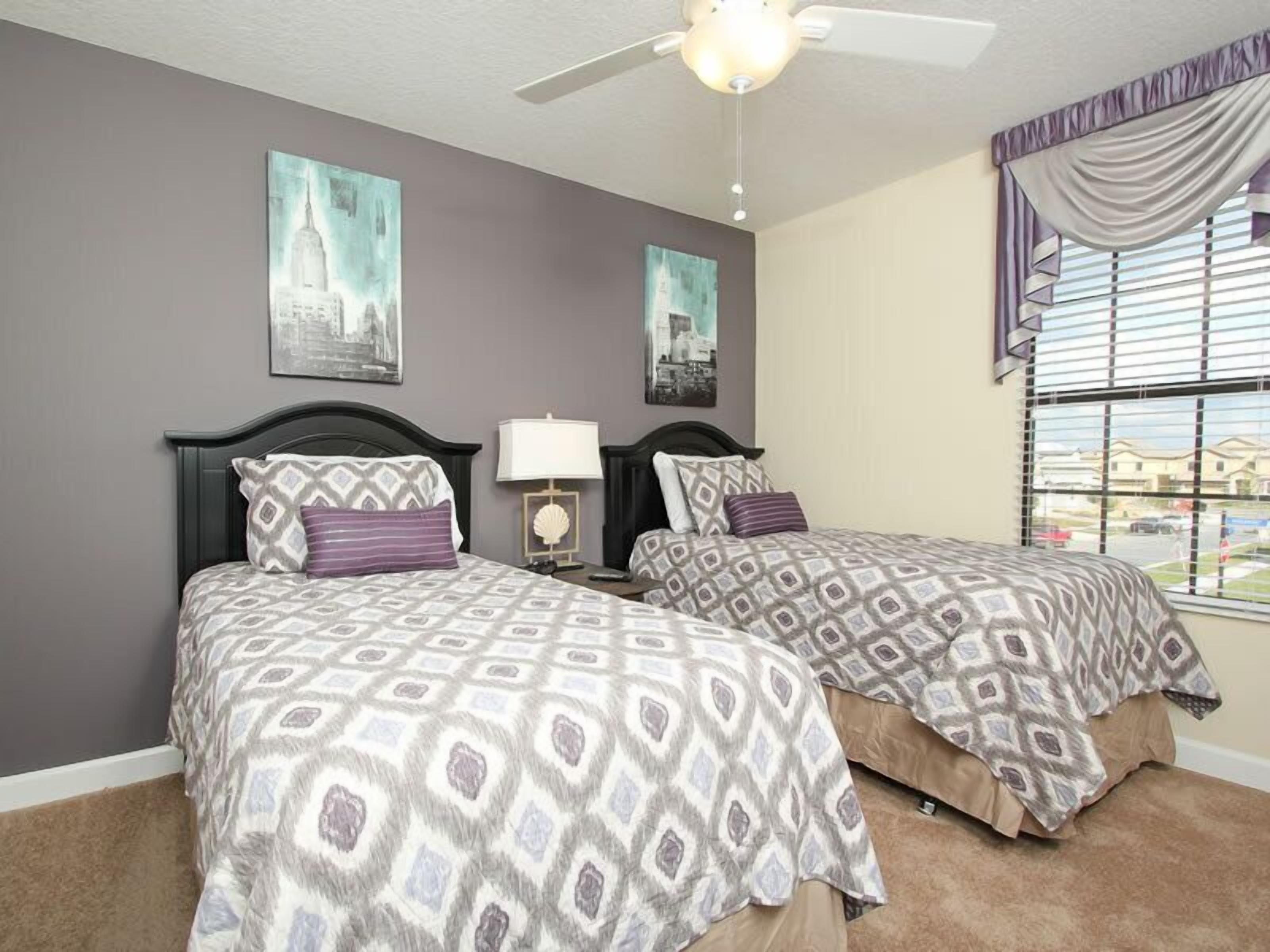 A bedroom with two beds, a ceiling fan, and two wall-mounted lamps.