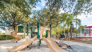 A playground with slides and climbing structures, surrounded by trees and a fenced area. - Ov2417 - Windsor Palms Resort - 6 Bed 3.5 Baths Villa (Kissimmee)